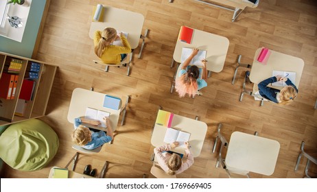 Elementary School Classroom: Children Sitting At Their School Desk Working On Assignments In Exercise Notebooks. Top View Shot.