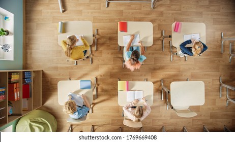 Elementary School Classroom: Children Sitting At Their School Desk Working On Assignments In Exercise Notebooks.Top View Shot.