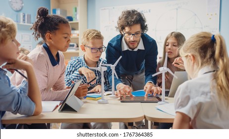 Elementary School Classroom: Enthusiastic Teacher Holding Tablet Computer Explains Lesson to Brilliant Young Children. Kids Learning Programming Languages, Internet Safety and Software Design - Shutterstock ID 1767364385