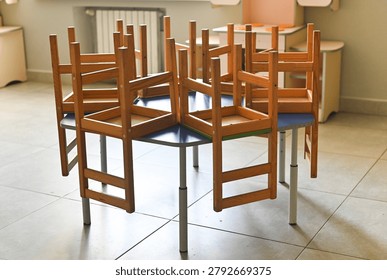 Elementary school classroom with tiny chairs on colorful desks, empty space with clean tiled floor, bright interior, organized and safe learning environment for kids