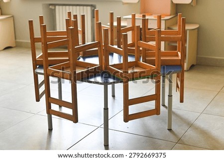 Elementary school classroom with tiny chairs on colorful desks, empty space with clean tiled floor, bright interior, organized and safe learning environment for kids