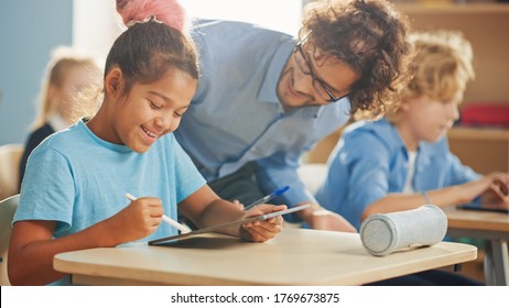 Elementary School Computer Science Class: Smart Girl Uses Digital Tablet Computer, Friendly Teacher Helps Her By Explaining Lesson And Asignment. Children Getting Modern Education