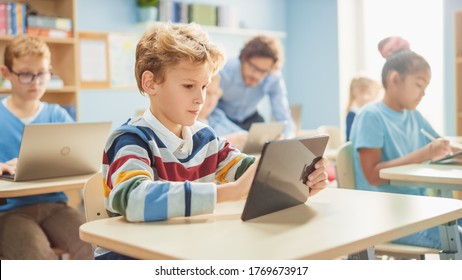 Elementary School Computer Science Class: Smart Boy Uses Digital Tablet Computer, His Classmates work with Laptops too. Children Getting Modern Education in STEM, Playing and Learning