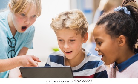 Elementary School Computer Science Class: Two Girls And Boy Use Digital Tablet Computer With Augmented Reality Software, They’re Excited, Full Of Wonder, Curiosity. Children In STEM, Playing, Learning