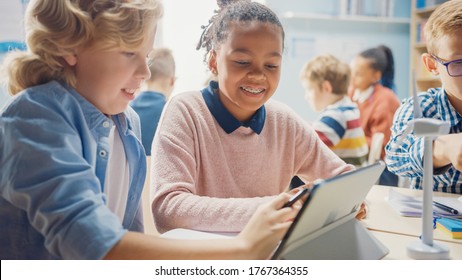 In the Elementary School: Girl and a Boy Work as a Team Using Tablet Computer. Diverse Classroom with Kids Learning Programming Language and Software Design