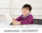 An elementary school girl, confident in her studies, operates a tablet with a smile on her face. Image of cram school and home study in Japan.