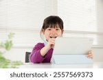 An elementary school girl happily operating a tablet while studying. Image of Asian children cramming and learning online.