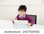 An elementary school girl happily operating a tablet while studying. Image of Asian children cramming and learning online.