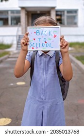 Elementary School Girl In Medical Mask Holds Picture With Back To School Message. First Offline Day With Social Distance Rules, New Normal Education, Reunion After Lockdown And Quarantine