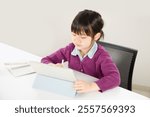 An elementary school girl studying while concentrating and operating a tablet. An image of Asian children studying at a cram school or online.