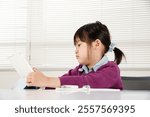 An elementary school girl with a tablet. She looks a little tired and looks at the screen. Image of cram school and online learning in Japan.