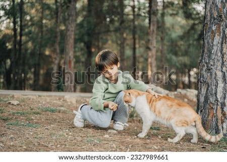 Elementary school kid petting feeding a stray cat in the city park. Child boy playing with abandoned homeless street cat in the forest.