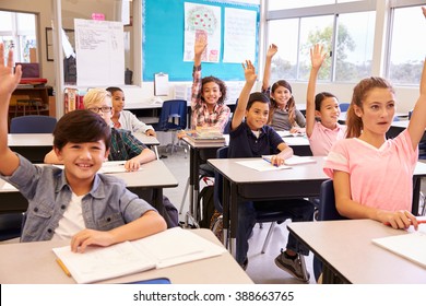 Elementary School Kids In A Classroom Raising Their Hands