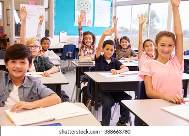 Elementary School Kids In A Classroom Raising Their Hands