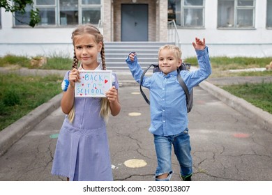 Elementary School Kids. Happy Girl Holds Picture With Back To School Message And Boy With Backpack Runs After First Offline Day, Study And Education, Reunion After Lockdown And Quarantine, Lifestyle