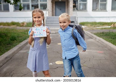 Elementary School Kids. Happy Girl Holds Picture With Back To School Message And Boy With Backpack Runs After First Offline Day, Study And Education, Reunion After Lockdown And Quarantine, Lifestyle