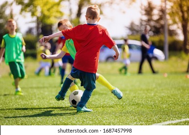 Elementary School Kids Playing Football In A Field. Boys Kicking Soccer On The Sports Grass Pitch. Children In Sportswear On Football Match
