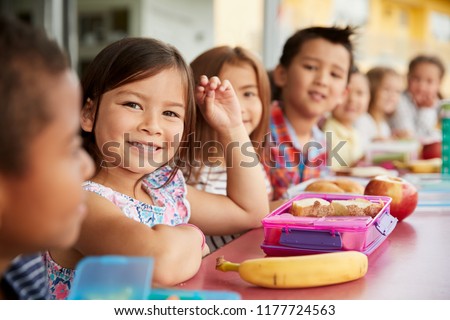 Elementary school kids sitting a table with  packed lunches