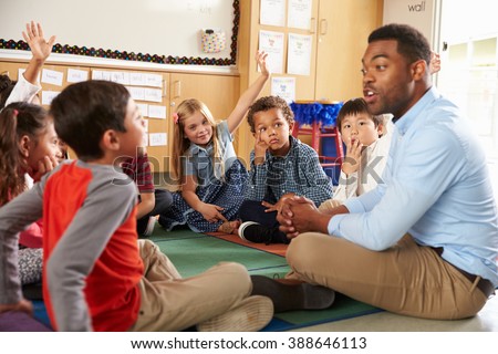 Elementary school kids and teacher sit cross legged on floor