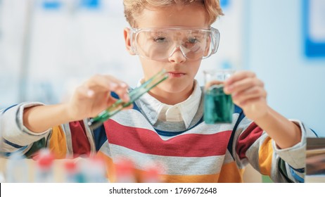 Elementary School Science or Chemistry Classroom: Smart Little Boy wearing Safety Glasses Mixes Chemicals in Beakers - Powered by Shutterstock