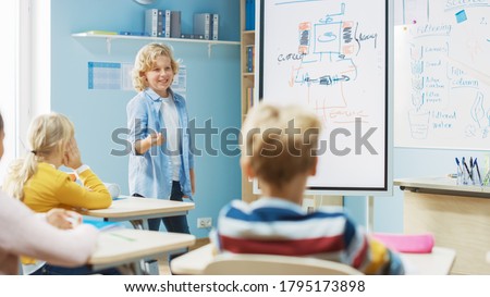 Elementary School Science Class: Cute Young Student Uses Interactive Digital Whiteboard to Show to a Classroom full of Classmates how Renewable Energy Works. Science Class, Curious Kids Listening