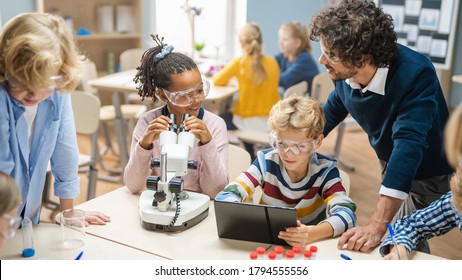 Elementary School Science Classroom: Cute Little Girl Looks Under Microscope, Boy Uses Digital Tablet Computer To Check Information On The Internet. Teacher Observes From Behind