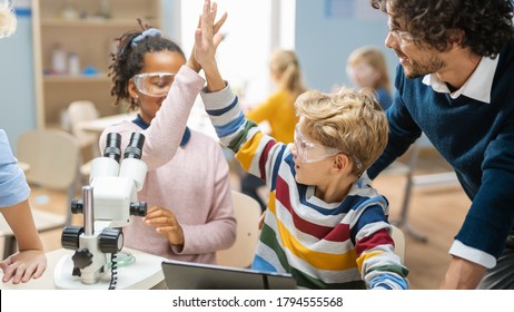 Elementary School Science Classroom: Cute Little Girl Looks Uses Microscope, Boy Uses Digital Tablet Computer To Check Information On The Internet And They Do High Five In Celebration.