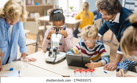 Elementary School Science Classroom: Cute Little Girl Looks Under Microscope, Boy Uses Digital Tablet Computer to Check Information on the Internet. Teacher Observes from Behind - Powered by Shutterstock