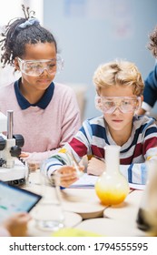 Elementary School Science Classroom: Cute Little Boy In Safety Glasses Mixes Chemicals In Beakers. Children Learn Chemistry Science With Interest