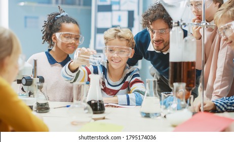 Elementary School Science Classroom: Little Boy Mixes Chemicals In Beakers. Enthusiastic Teacher Explains Chemistry To Diverse Group Of Children. Children Learn With Interest