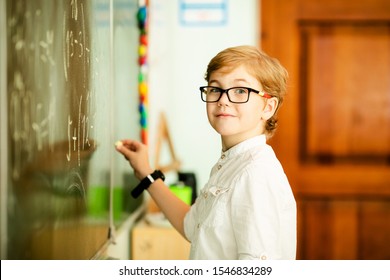 Elementary School Student With Black Glasses Writing Maths Answer On Chalkboard.