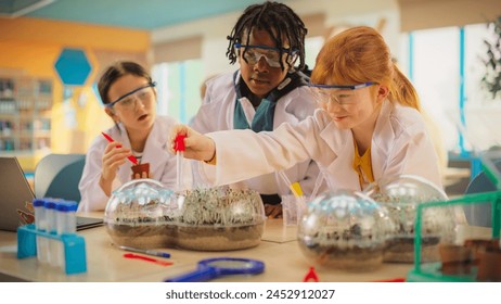 Elementary School Students Sitting Behind a Table in a Group, Conducting a Biology Experiment for a Science and Technology Fair. Young Boys and Girls Wearing Protective Clothes and Goggles - Powered by Shutterstock