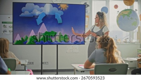 Elementary School Students Studying Basic Information About Weather Factors in Modern Classroom. Female Teacher Explaining Water Cycles to Smart Kids During Geography Lesson Using Digital Screen.
