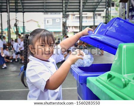 Elementary school students are throwing garbage into the bin with a smiling face.