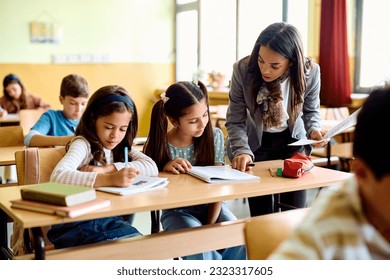 Elementary school teacher assisting schoolgirl's on a class in the classroom. - Powered by Shutterstock