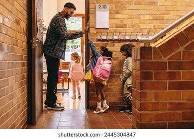 Elementary school teacher greeting his students at the door. Male teacher welcoming his class with a high five outside their classroom. Child mentor motivates his pupils in a primary school.