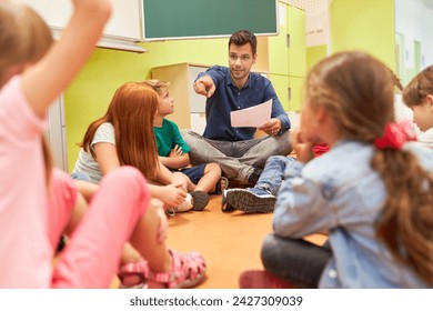 Elementary school teacher sitting in circle with group of students in classroom - Powered by Shutterstock