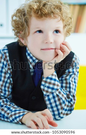 Elementary schoolboy thinking while doing homework in classroom, staring into the distance propping up his head