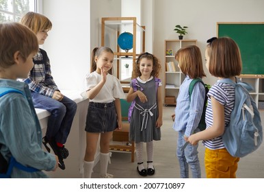 Elementary Schoolchildren Group Talking During Break Standing In Classroom. Pupils Engaged In Homework Discussion. Children Spending Time Together During Recess Between Lessons, Speaking Having Fun