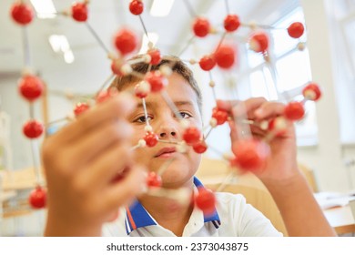 Elementary schoolkid analyzing molecular structure while sitting in classroom