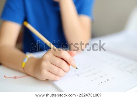 Elementary student boy doing homework at home. Child learning to count, solves arithmetic examples, doing exercises in workbook. Math tutorial. Preparing preschooler baby for school.Education for kids