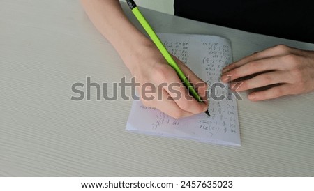 Elementary student boy doing homework at home. Child learning to count, solves arithmetic examples, doing exercises in workbook. Math tutorial.