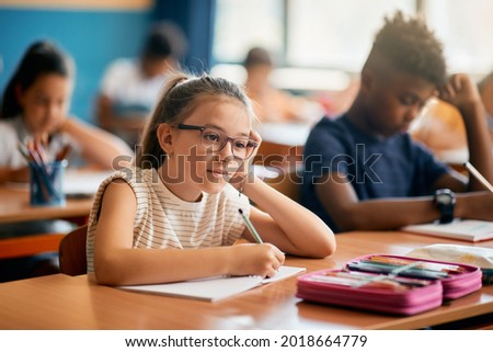 Elementary student feeling bored while writing in her notebook during a class at school.