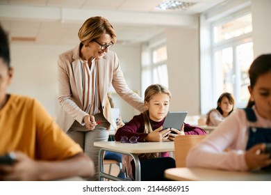 Elementary student using digital tablet while her teacher is assisting her in the classroom.  - Powered by Shutterstock