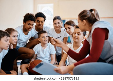 Elementary students listening their basketball coach during physical education class at school gym. - Powered by Shutterstock