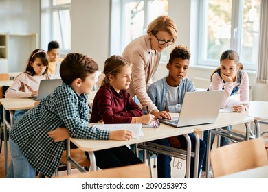Elementary teacher and her students using laptop during computer class at school.