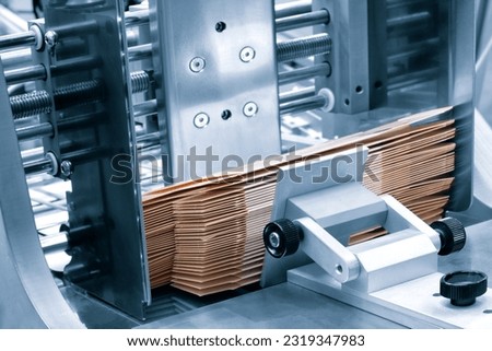 Elements of corton boxes are collected in stack. Conveyor line for the production of boxes. Machine cuts cardboard boxes from sheets of cardboard. Enterprise for the production package.