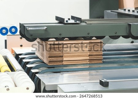 Elements of corton boxes are collected in stack. Conveyor line for the production of boxes. Machine cuts cardboard boxes from sheets of cardboard. Enterprise for  production package.