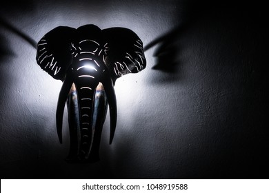 Elephant head lit from behind. Object hanging on the wall.