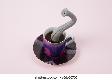 An elephant trunk emerging from a small design cup of coffee as if he were hiding. Minimal funny and quirky design still life photography
